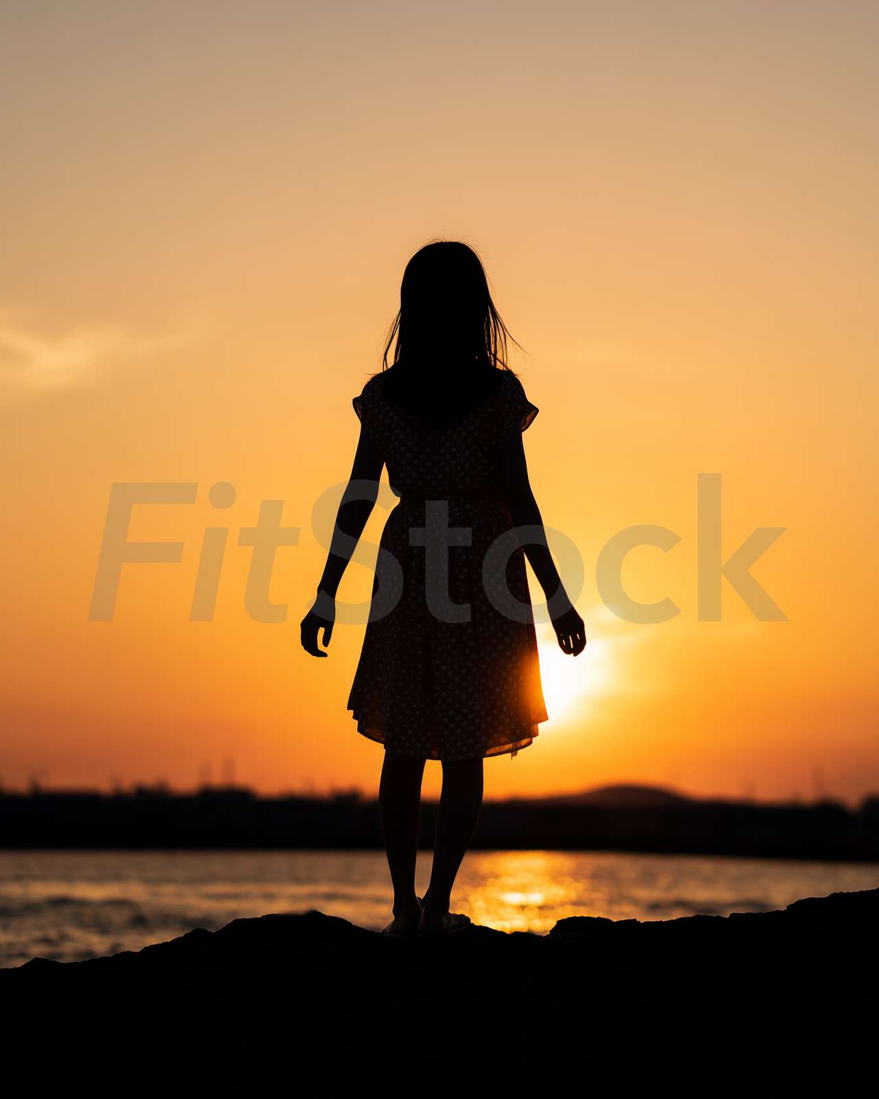 夕暮れの海辺に佇む少女のシルエット