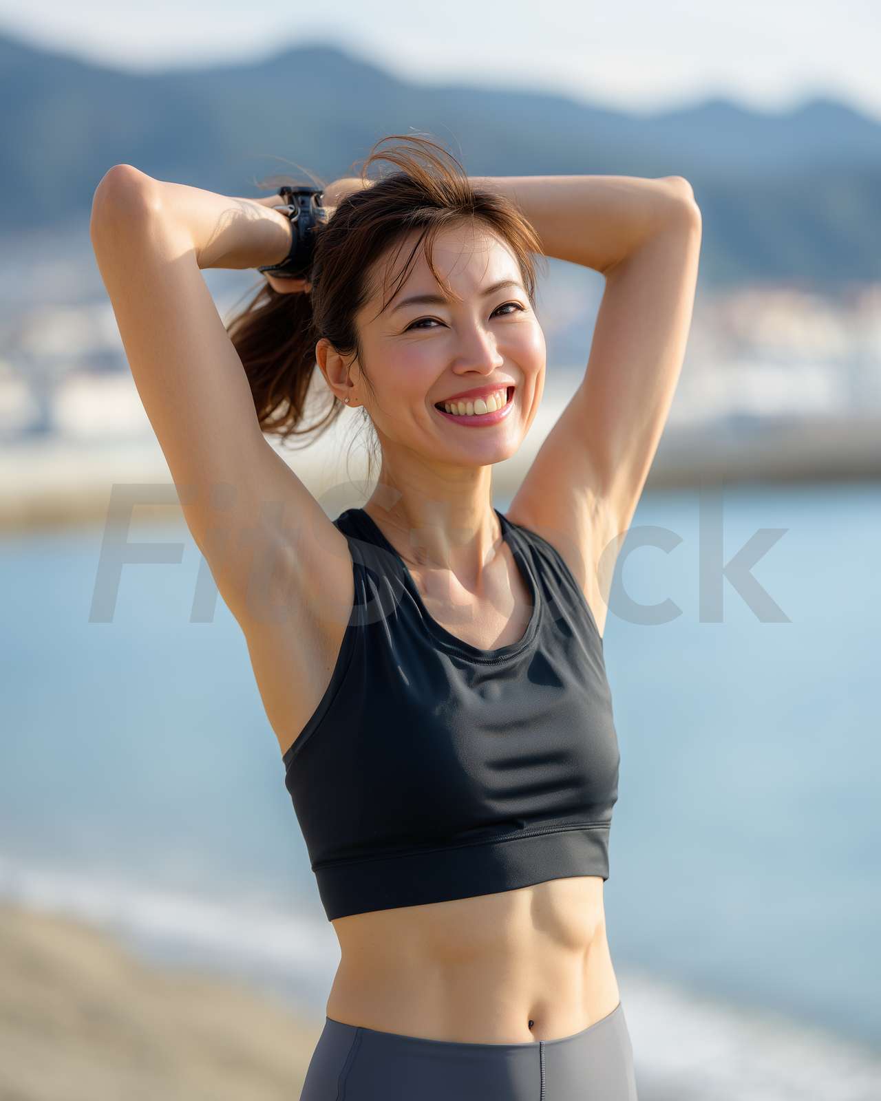 海辺で髪を結ぶ笑顔の女性