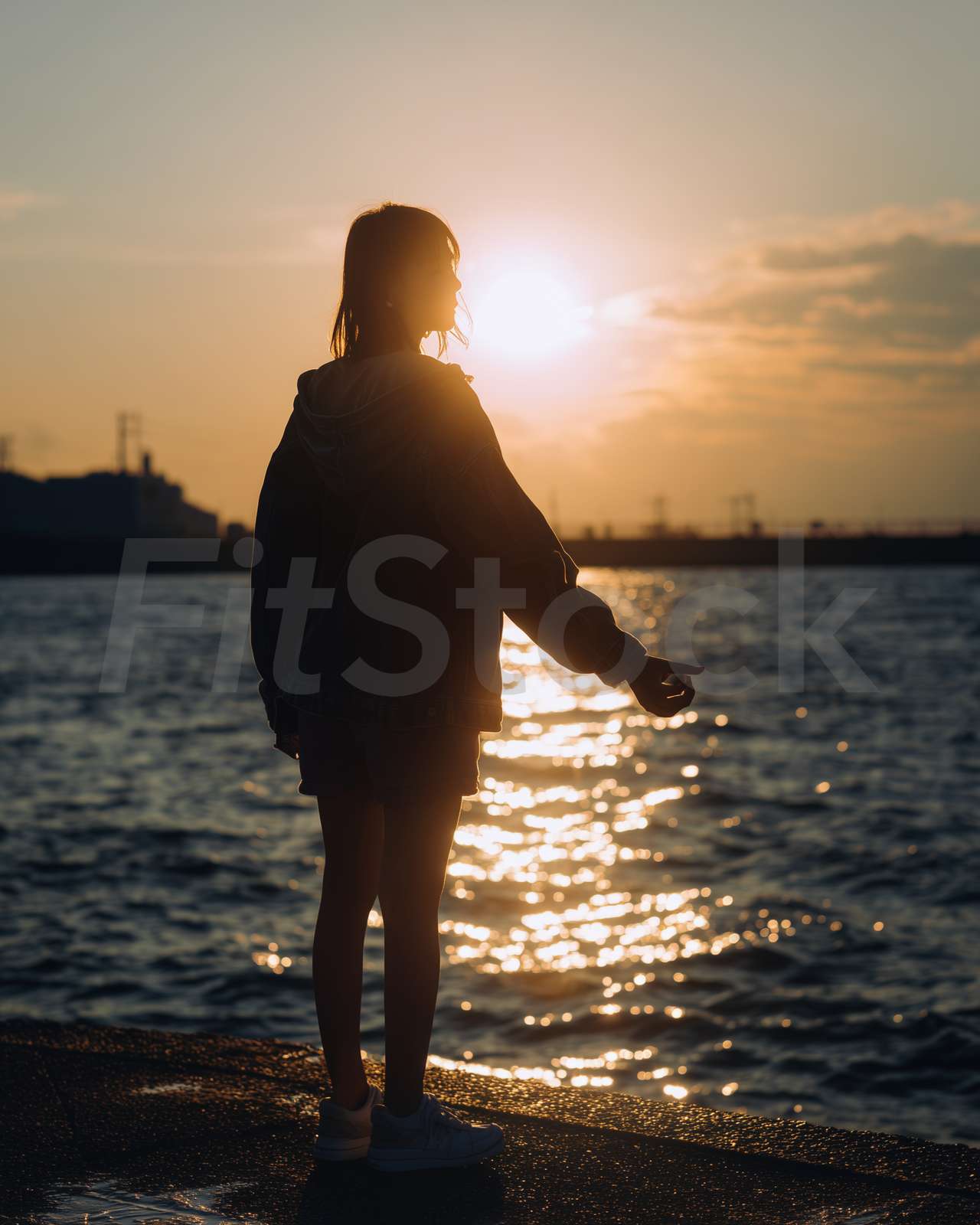 夕暮れの海辺に立つシルエットの女性