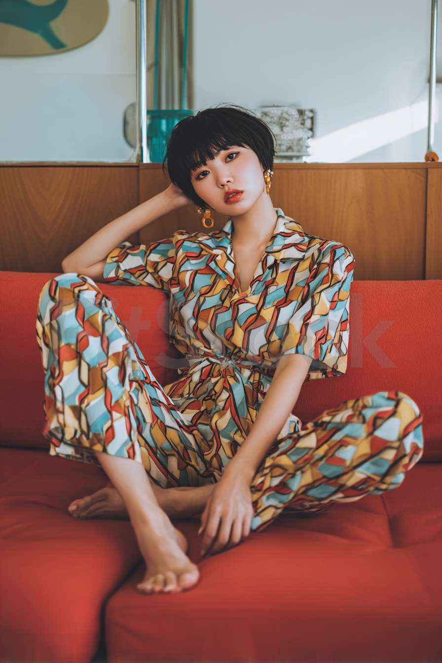 赤いソファでくつろぐ個性的なプリントのセットアップを着た女性