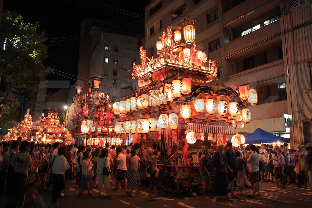 夜の街を練り歩く豪華な山車と祭りの人々