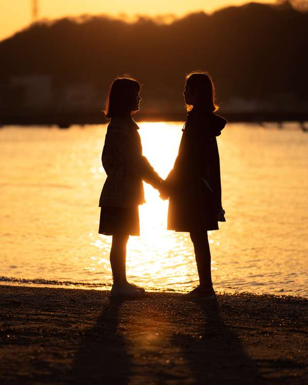 夕暮れの海岸で手を繋ぐ二人の女性のシルエット