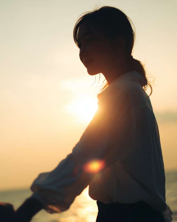 夕暮れの海辺で穏やかに微笑む女性のシルエット