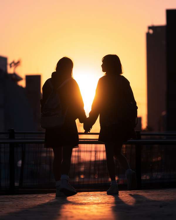 夕暮れ時に手をつないで歩く女子学生のシルエット