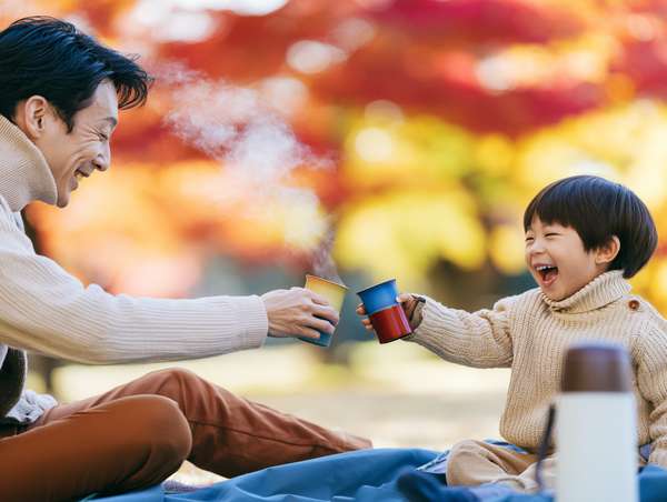 紅葉の中で温かい飲み物を楽しむ父と子