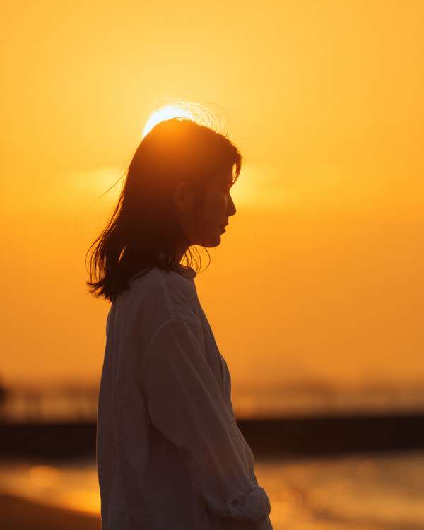 夕日を背景に佇む女性の横顔シルエット