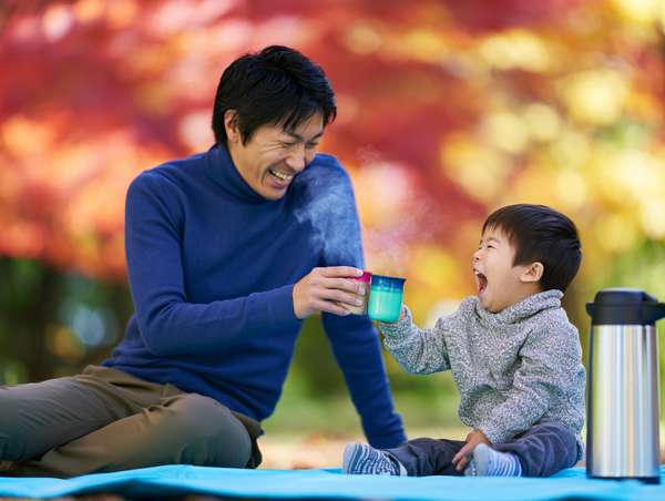 紅葉の下で温かい飲み物を楽しむ親子