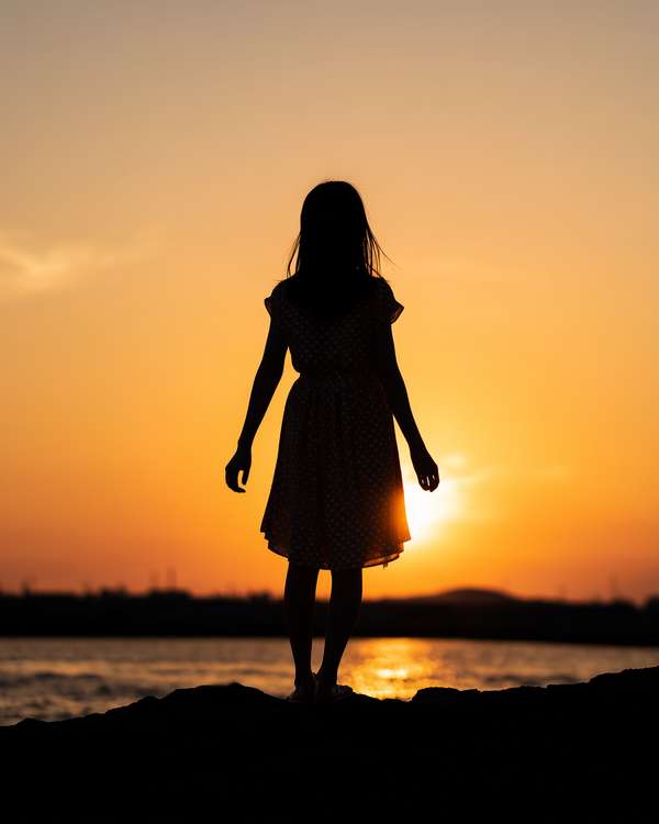 夕暮れの海辺に佇む少女のシルエット