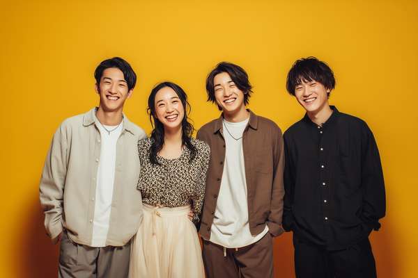 黄色い背景で笑顔を見せる4人の若者グループ