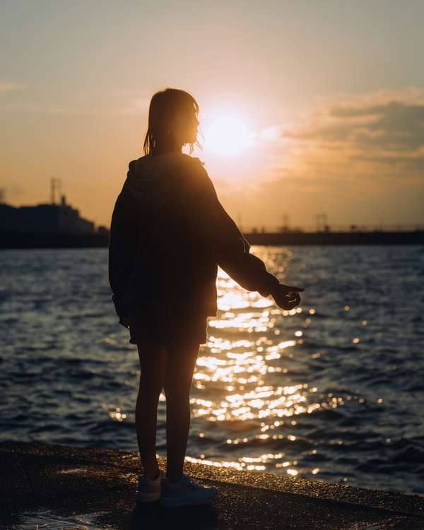 夕暮れの海辺に立つシルエットの女性