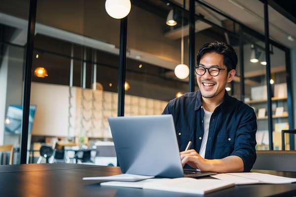オフィスで笑顔でPC作業をするアジア人男性