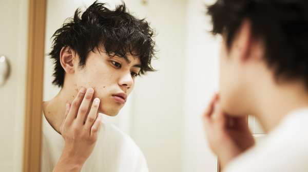 鏡を見て肌の状態を確認する若い男性