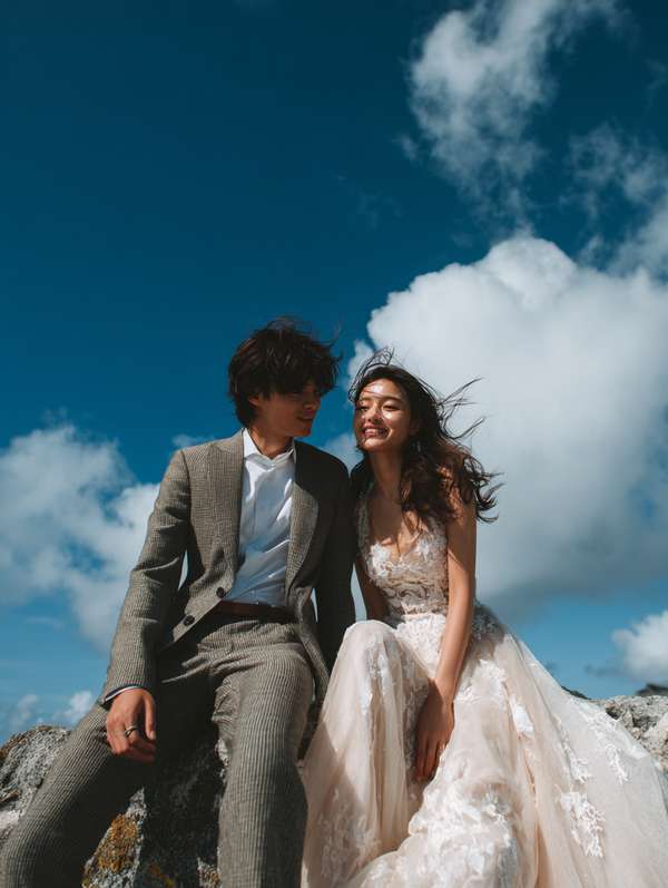 青空の下、岩場で微笑む幸せな結婚式カップル