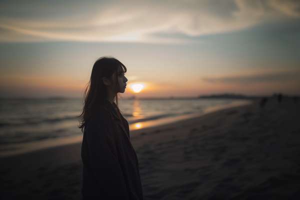 夕暮れの海辺で佇む女性