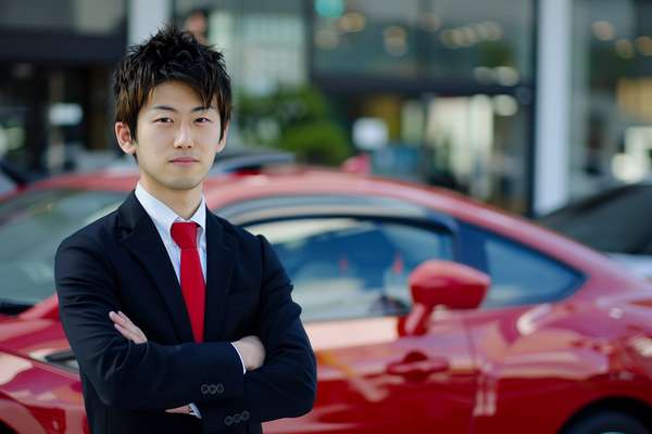 赤い車の前で腕を組む日本人男性セールスマン