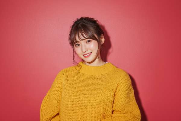 赤い壁を背景に黄色いセーターを着て微笑む若い女性