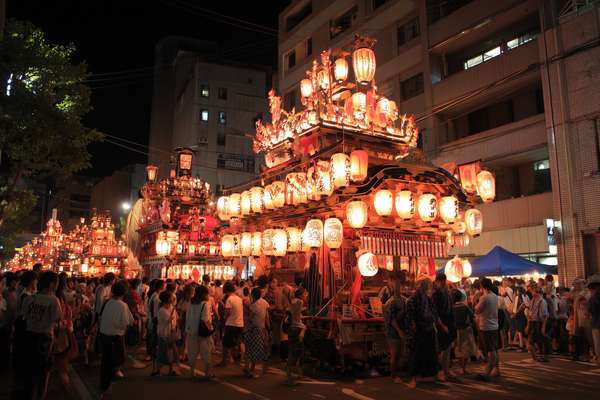 夜の街を練り歩く豪華な山車と祭りの人々