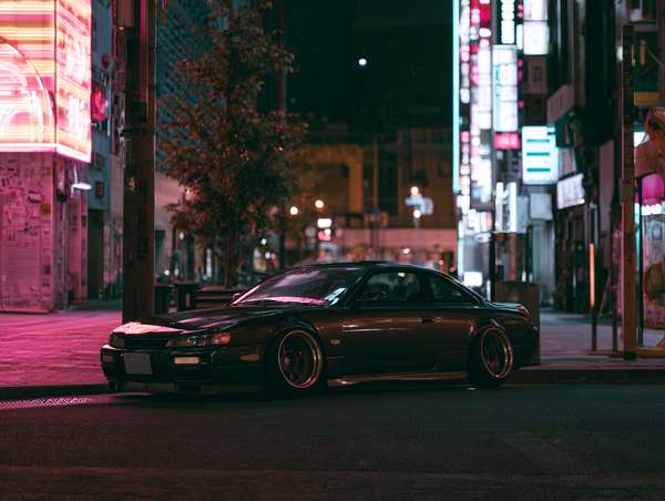 ネオン輝く夜の街に佇むスポーツカー