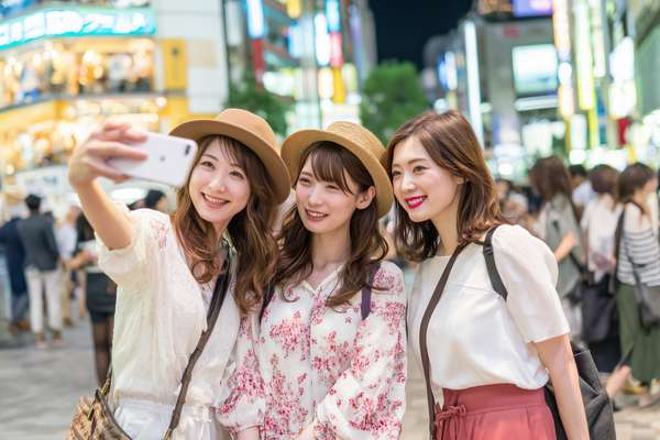 都会の夜、スマホで自撮りをする楽しそうな女性グループ