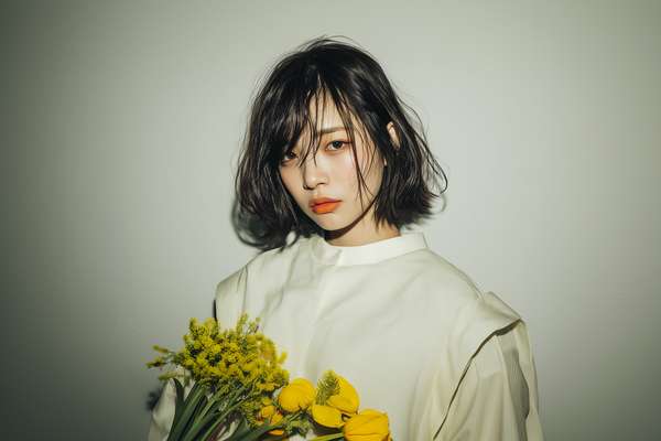 黄色い花を持つクールな表情の女性