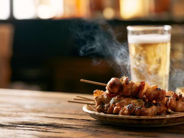 湯気が立つ焼き鳥と冷えたビールの組み合わせ