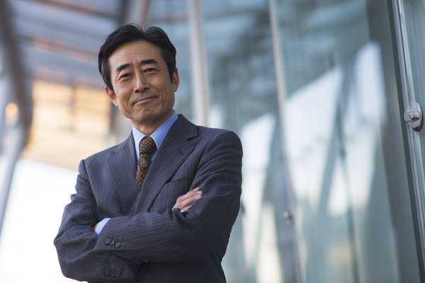 オフィスビルの前で腕を組む自信に満ちた日本人ビジネスマン