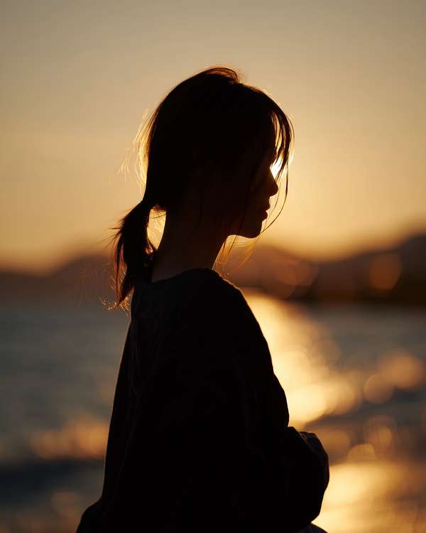 夕暮れの海辺でたたずむ女性のシルエット