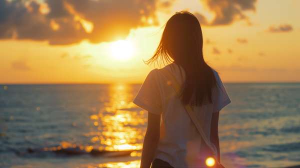 夕暮れの海辺に立つ少女の後ろ姿