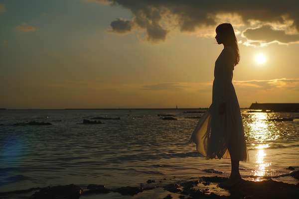夕暮れの海辺に立つ女性のシルエット